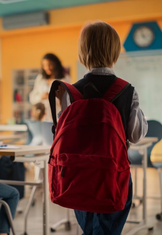 student with red backpack walking into a classroom in river falls school