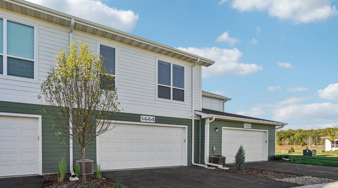 Modern townhome exterior with attached garages labeled 1444 and 1450 under a blue sky.
