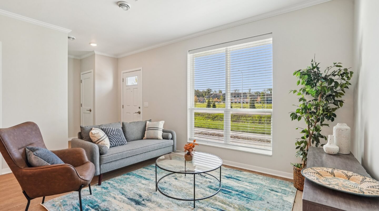 Bright living room with modern furniture, large window, and teal area rug in a two-bedroom townhome.