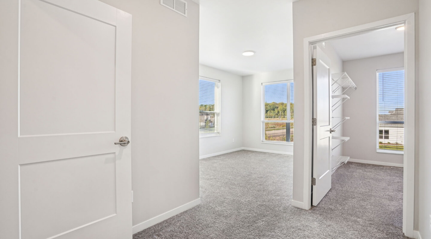 Bright upstairs bedroom with carpet flooring and connected walk-in closet in a modern townhome.
