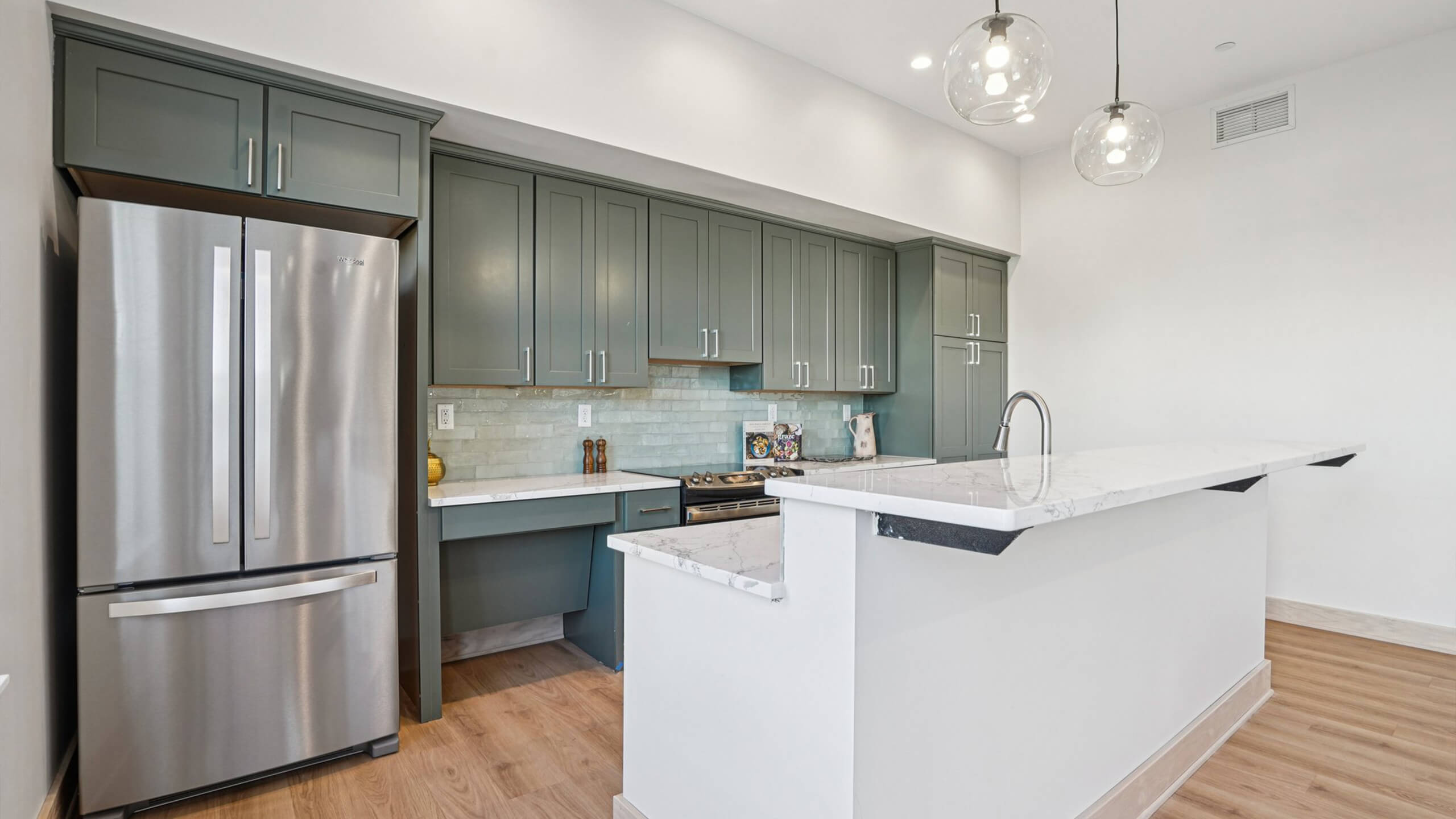 Clubhouse kitchen with green cabinetry, stainless steel refrigerator, and marble countertops.