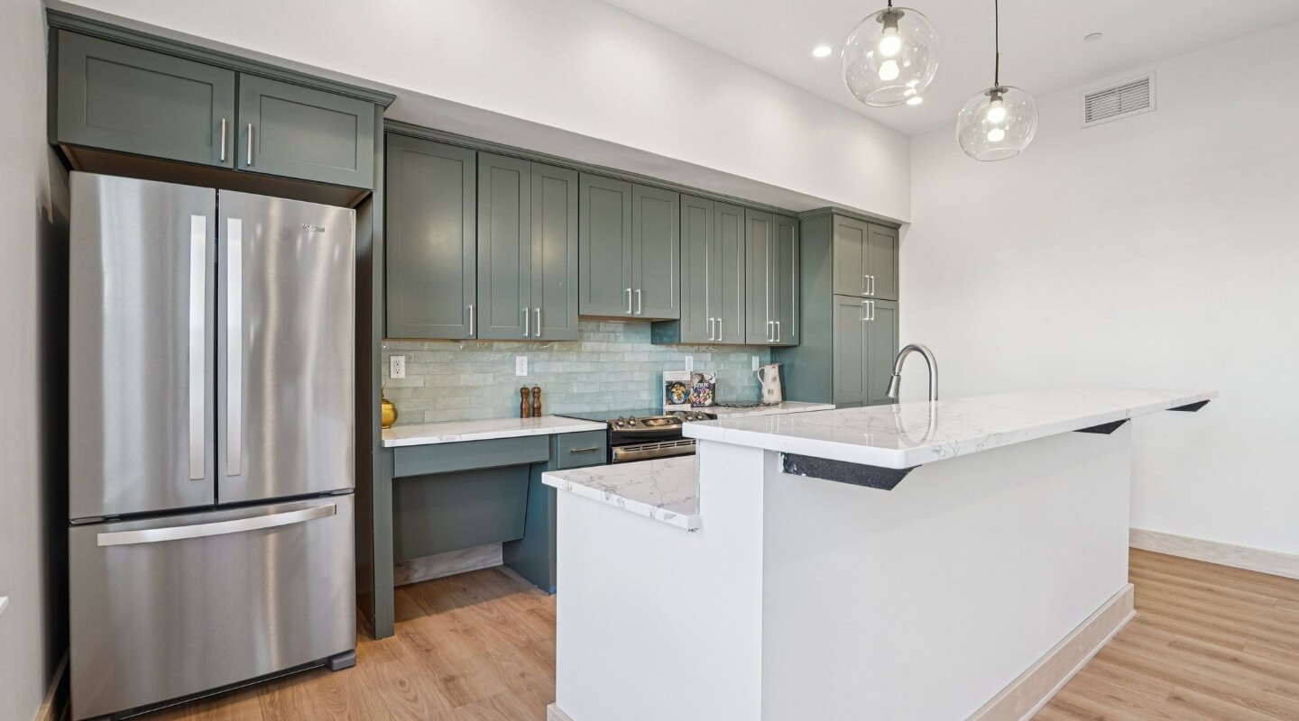 Modern clubhouse kitchen featuring green cabinetry, marble countertops, and stainless steel appliances.