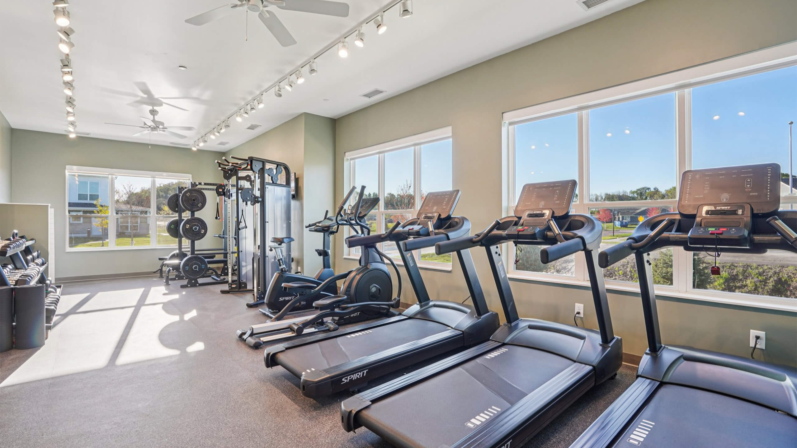 Bright community fitness room with treadmills, weight racks, and large windows.