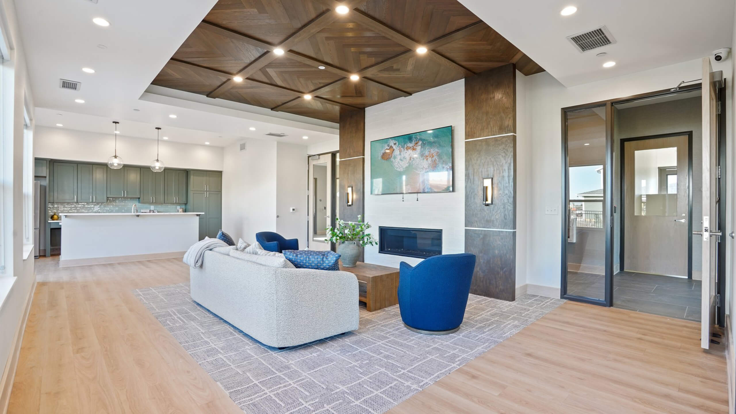 Spacious community lounge with wood ceiling design, fireplace, and open layout connected to the kitchen.