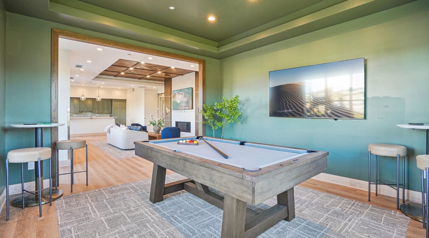 Clubhouse game room featuring a pool table, bar seating, and adjoining lounge area.