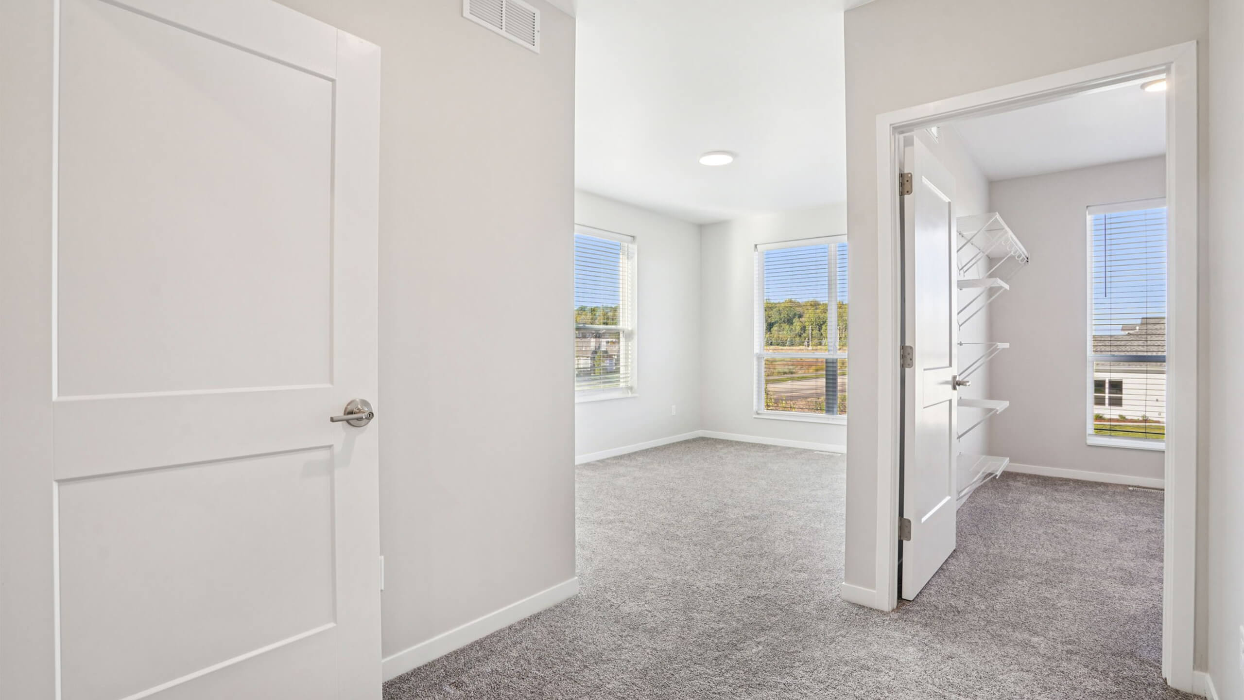 Upstairs bedroom and closet area with neutral carpet, white doors, and large windows.