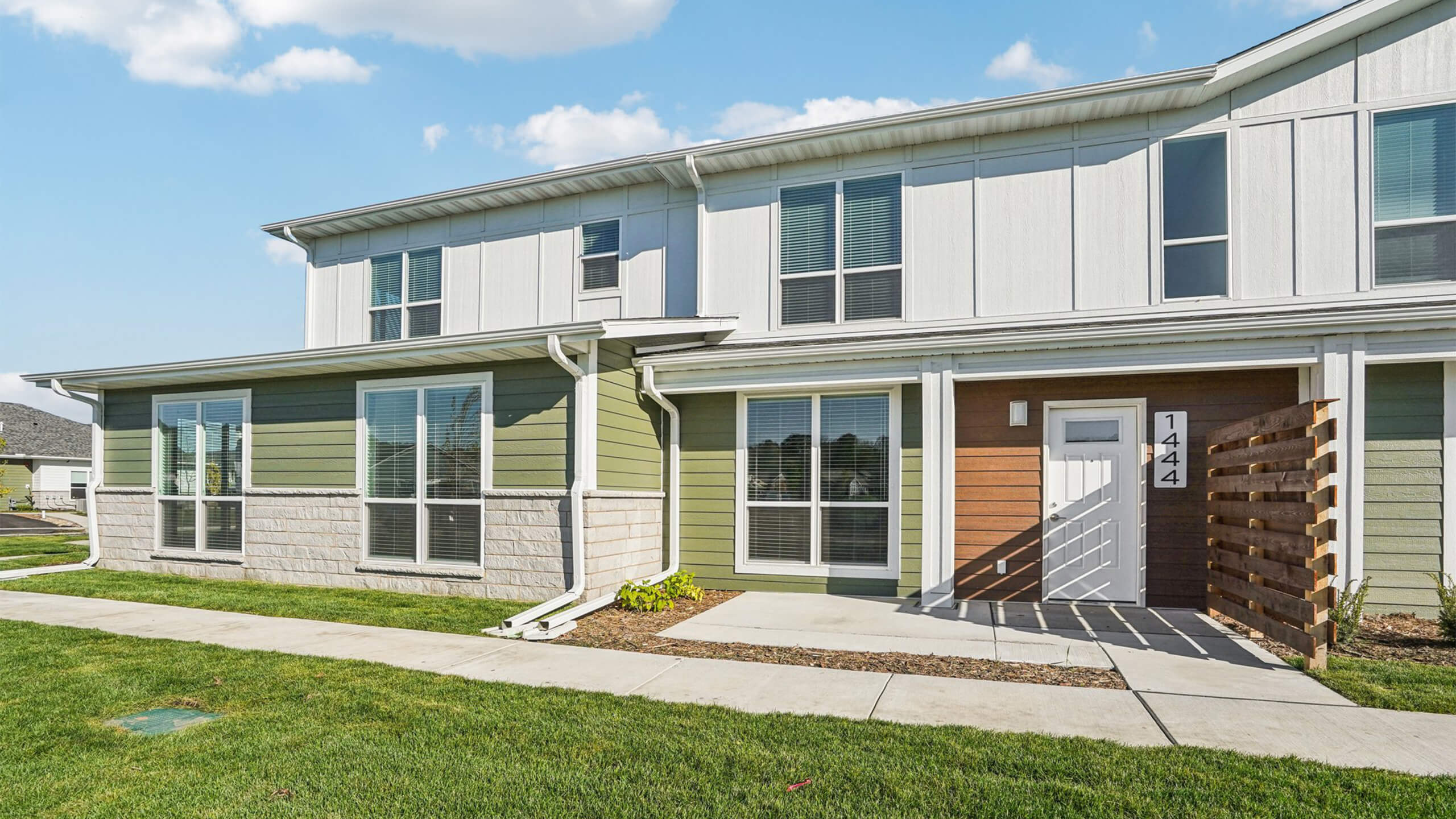 Modern townhome exterior with white and green siding, stone accents, and a private entry for unit 1444.