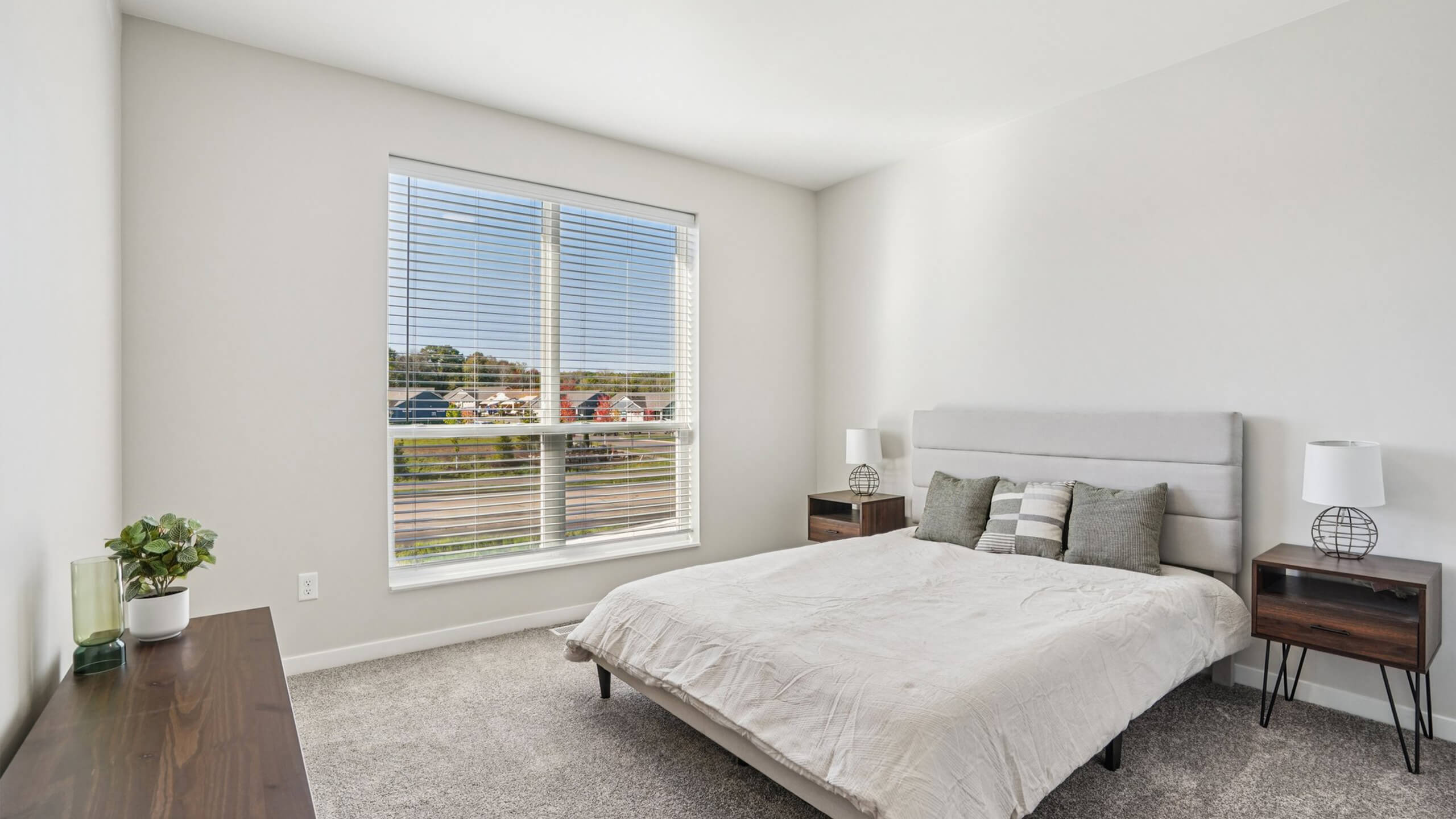 Primary bedroom with minimalist design, soft gray tones, and large window view.