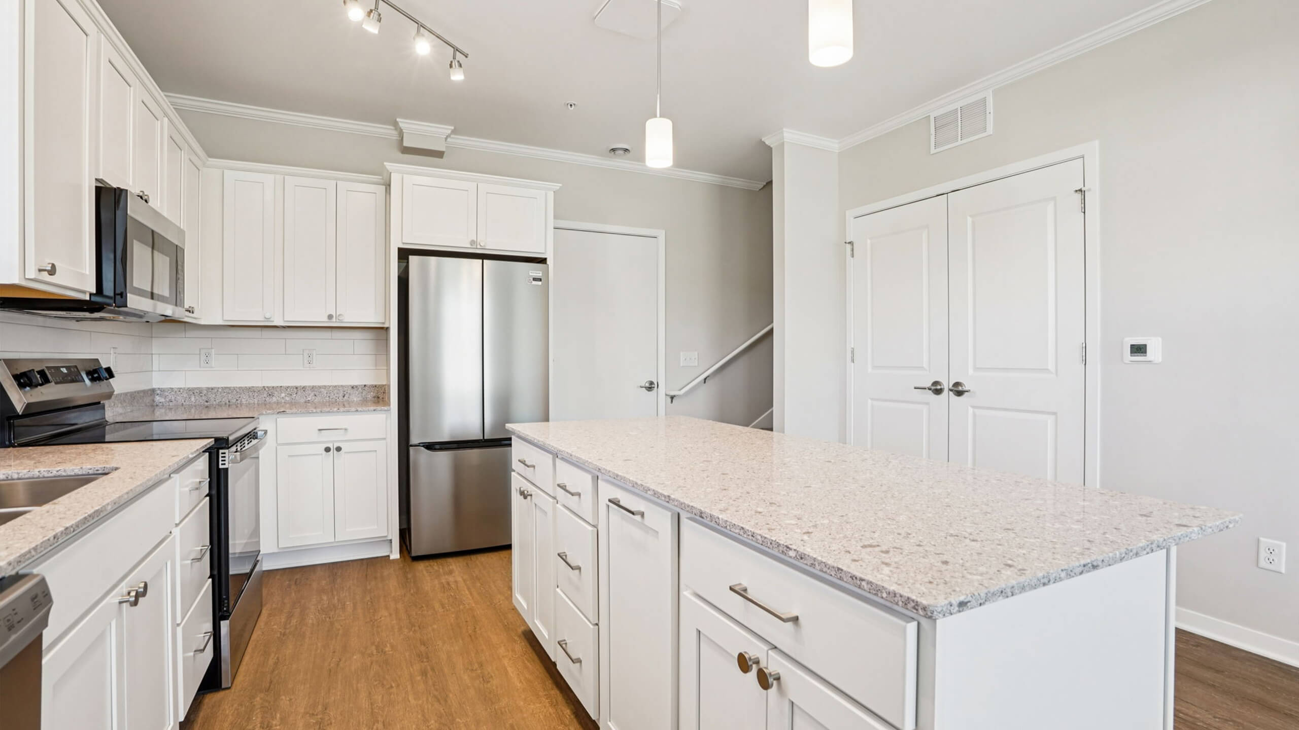 Spacious kitchen featuring white cabinetry, stainless steel appliances, and a large island with pendant lighting.